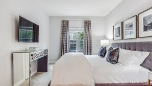 A modern hotel room with a large bed, a desk, a flat-screen TV, and a window with patterned curtains. - Picture Perfect (Atlanta)