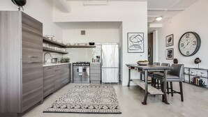 A modern kitchen with stainless steel appliances, a dining area with a wooden table and chairs, and a patterned rug. - Clock Loft (Atlanta)