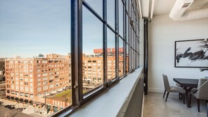A high-rise apartment with large windows offering a city view, a dining area with a table and chairs, and a framed abstract painting on the wall. - Clock Loft (Atlanta)