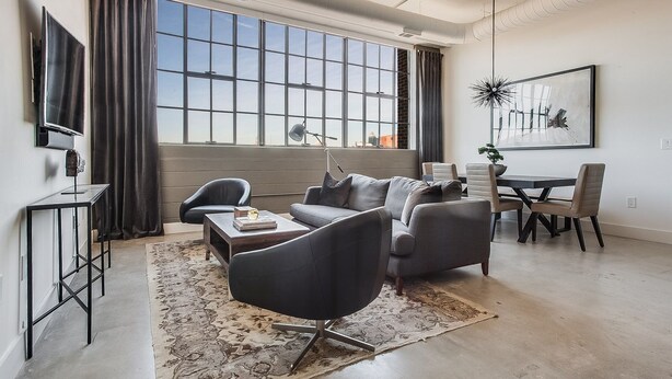 A modern living room with a sofa, armchairs, a coffee table, and a dining area with a table and chairs. - Clock Loft (Atlanta)