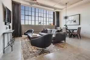 A modern living room with a sofa, armchairs, a coffee table, and a dining area with a table and chairs. - Clock Loft (Atlanta)