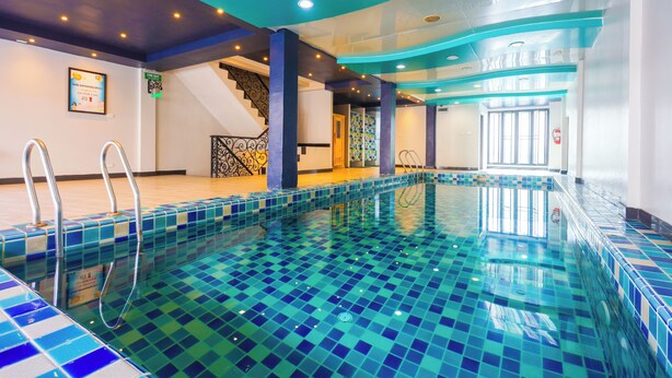 A swimming pool with blue and green mosaic tiles, a staircase with a black railing, and a staircase with a white railing. - Land Royal Residence (Pattaya)