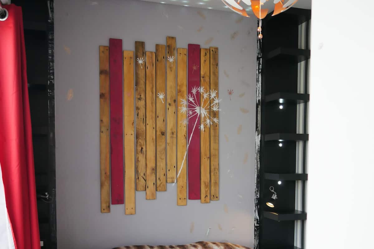 Une chambre à coucher avec un lit, un mur recouvert de panneaux en bois, un luminaire suspendu et une fenêtre avec des stores.