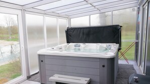 Un moderno spa con un jacuzzi, un taburete y vistas a un paisaje verde a través de amplios ventanales.