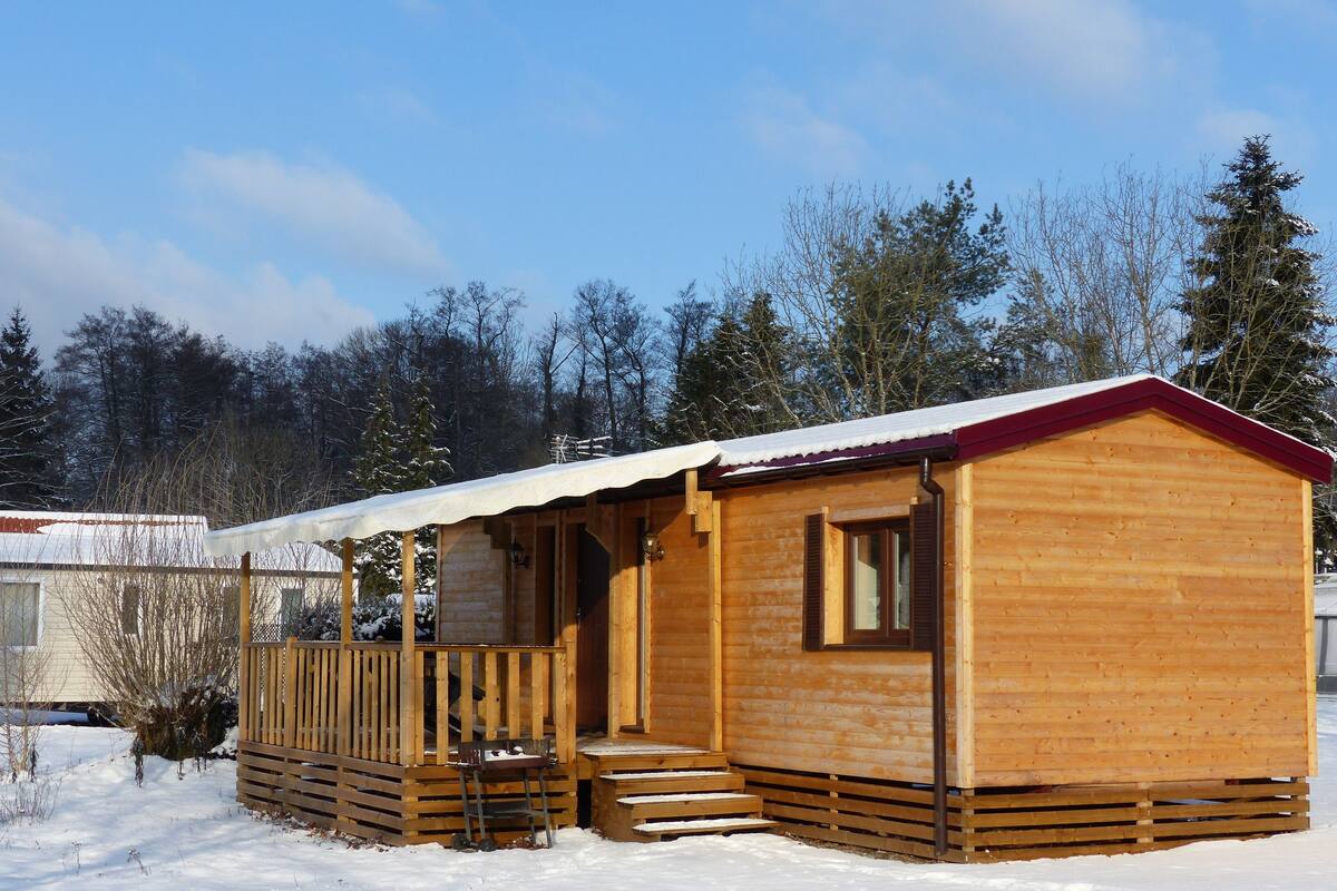 Une cabane en bois dotée d’un porche et d’un escalier menant à l’entrée, entourée de neige et d’arbres.