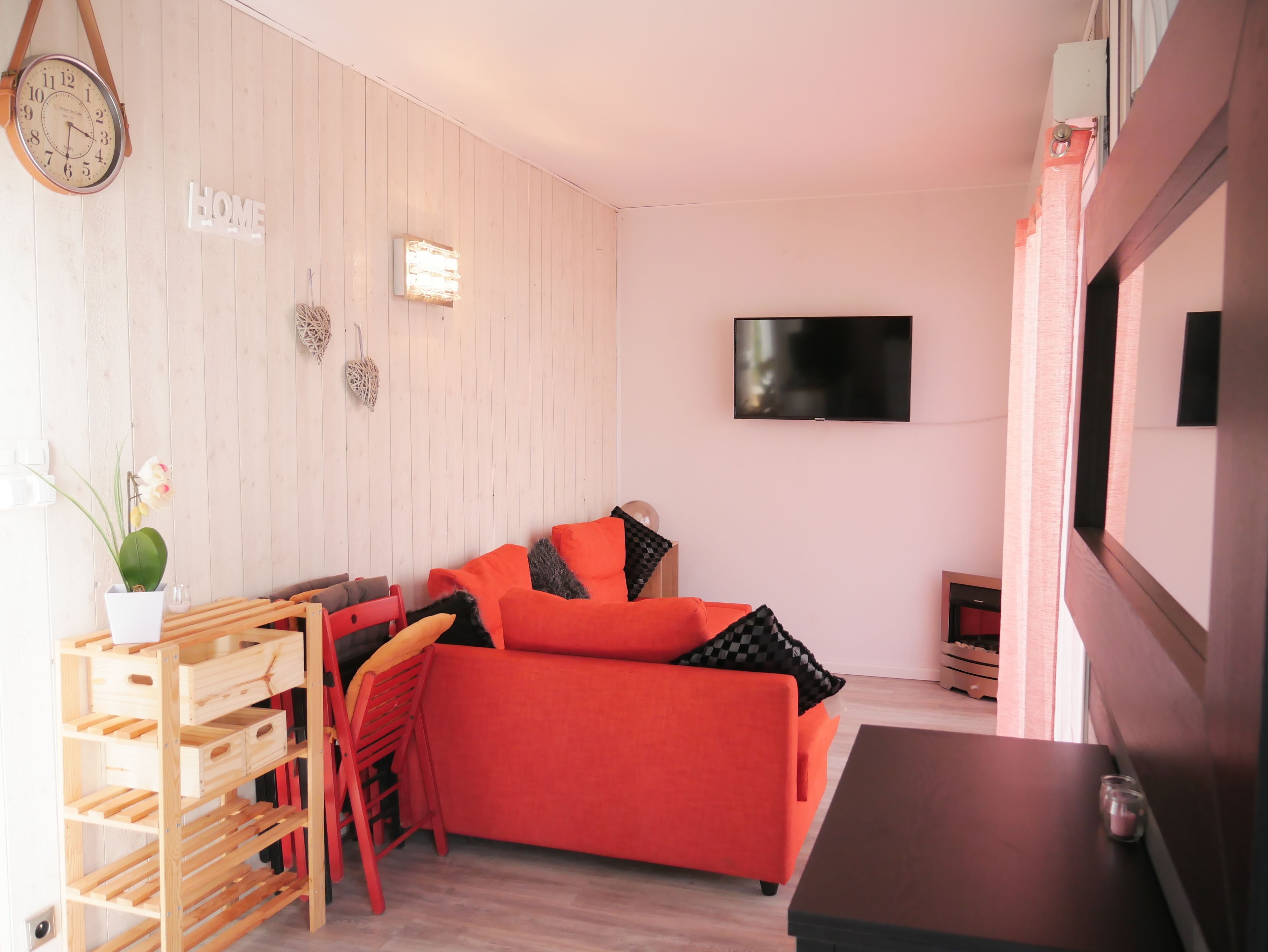 A cozy room with a wooden wall, a red sofa, a wooden side table, and a TV mounted on the wall.