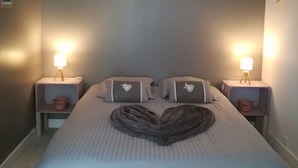 Ein ordentlich bezogenes Bett mit Kissenanordnung im Herzen-Design, zwei Nachttischlampen und einer Wandleuchte.