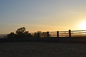 Un coucher de soleil sur une zone délimitée par une clôture, dont le sol est sablonneux.