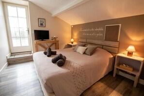 Une chambre à coucher comprenant un lit, des tables de chevet, un téléviseur et un mur orné d’une citation.