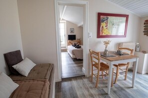 Une pièce comprenant un lit, une table à manger en bois avec des chaises, un téléviseur en arrière-plan et un tableau accroché au mur.