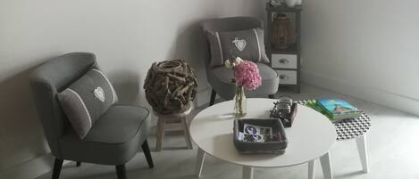 Un salón moderno con un sofá gris, una mesita redonda y un elemento decorativo en la pared.