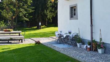A patio with a table and chairs, surrounded by potted plants and a stone bench.