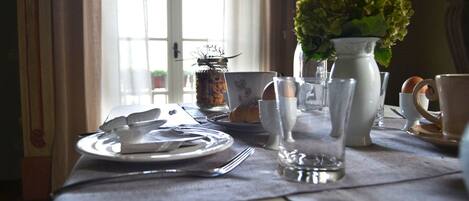 A dining table set with plates, cutlery, and glassware, with a vase of flowers and a candle holder in the background.