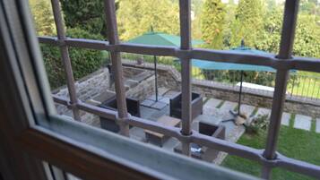 A view through a metal gate of an outdoor patio area with stone steps, planters, and a green umbrella.