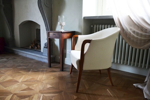 A room with a herringbone wood floor, a white armchair, a small wooden table with a glass object, and a radiator. - B&B Dimora delle Donnole (Bergamo)