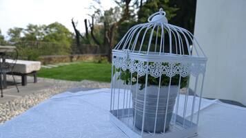 En hvid metalfuglebur med en plante på et hvidt borddække udendørs.