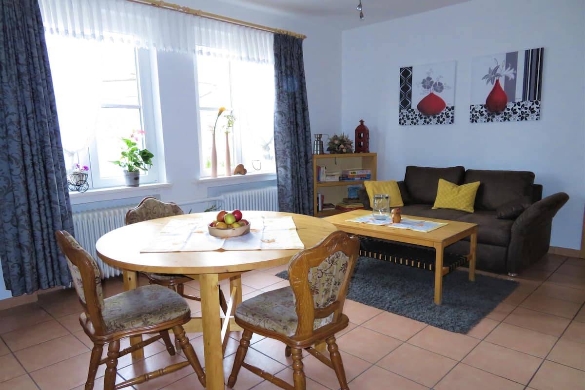 A dining area with a round table and four chairs, a sofa, a bookshelf, and a radiator.