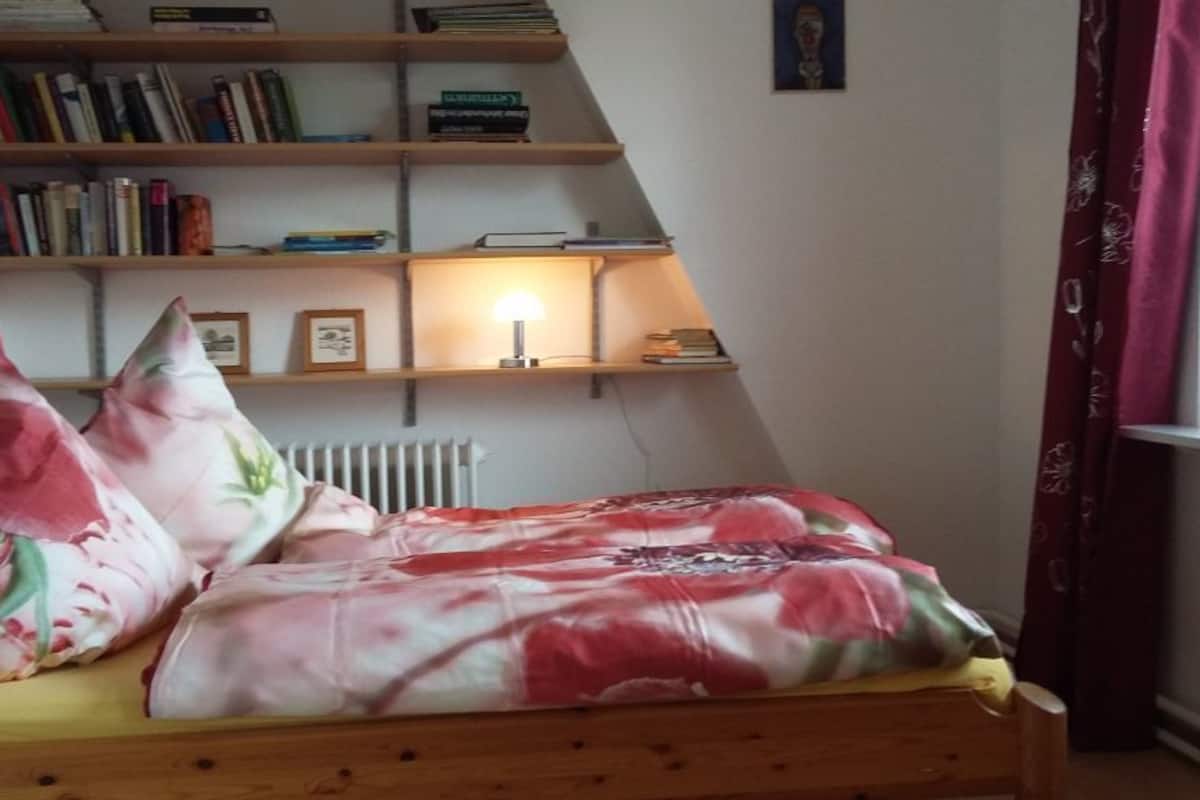 A bedroom with a wooden bed, floral pillows, a bookshelf, and a radiator.