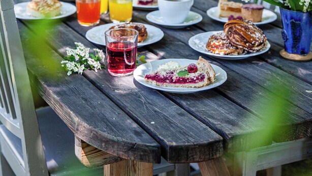 A wooden picnic table set outdoors with plates of food, cups, and a pitcher of red drink. - STF Sala Silvergruva (Sala)