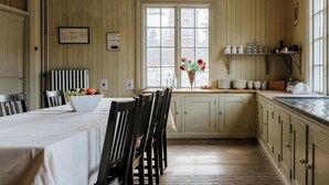 A kitchen with wooden cabinets, a dining table with chairs, a fruit bowl, and a window with a view of buildings. - STF Sala Silvergruva (Sala)