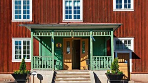 A wooden building with a green porch, steps leading to the entrance, and two wheelbarrows with plants. - STF Sala Silvergruva (Sala)