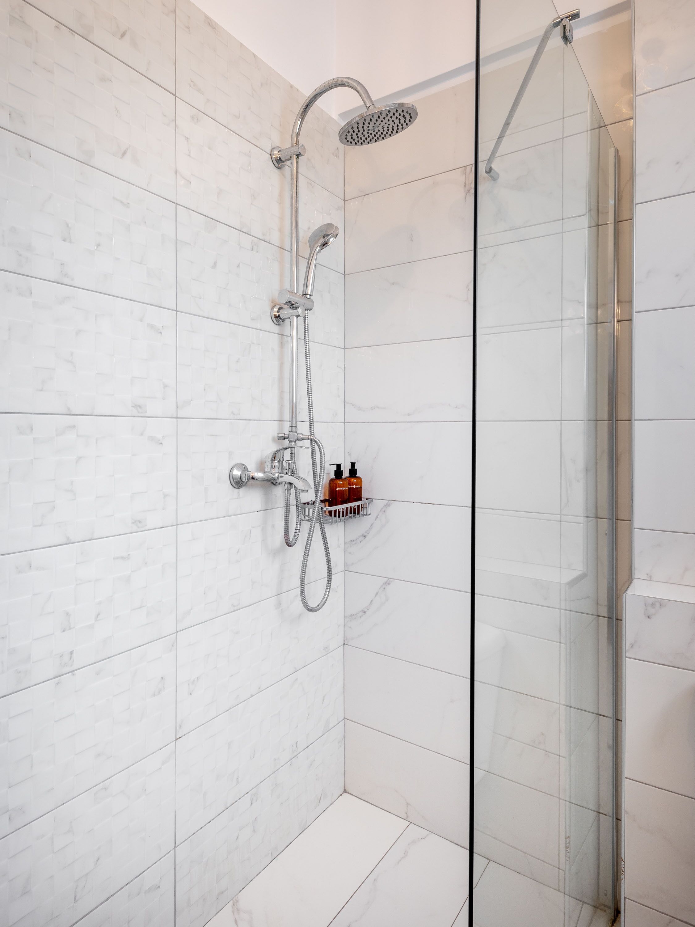 A modern shower with a glass enclosure, a handheld showerhead, and a wall-mounted faucet.