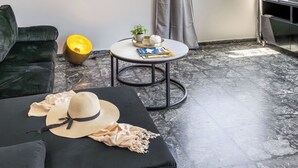 A modern living room with a black sofa, a round coffee table with a plant, a television, and a view of the sea. - Seaside Secret by BluPine (Vari-Voula-Vouliagmeni)