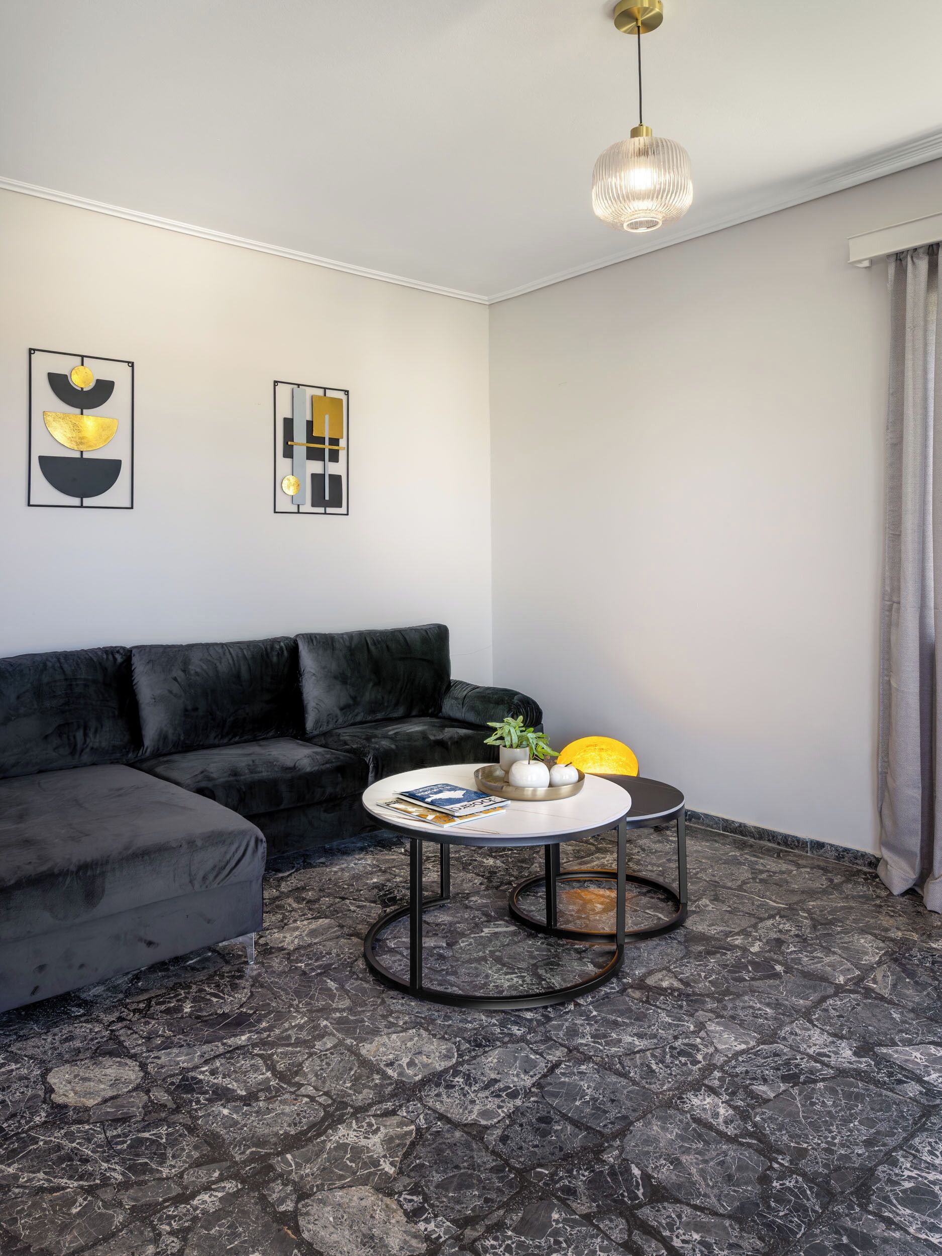 A modern living room with a black sectional sofa, a round coffee table with magazines and a plant, and abstract wall art.