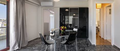 A modern dining area with a glass table, black chairs, and a fruit bowl.