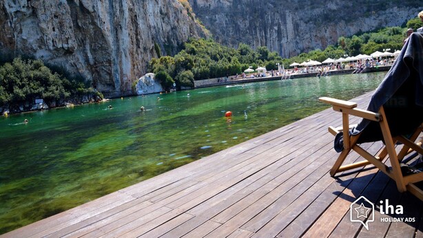 A wooden deck overlooking a clear body of water with cliffs in the background. - Seaside Secret by BluPine (Vari-Voula-Vouliagmeni)