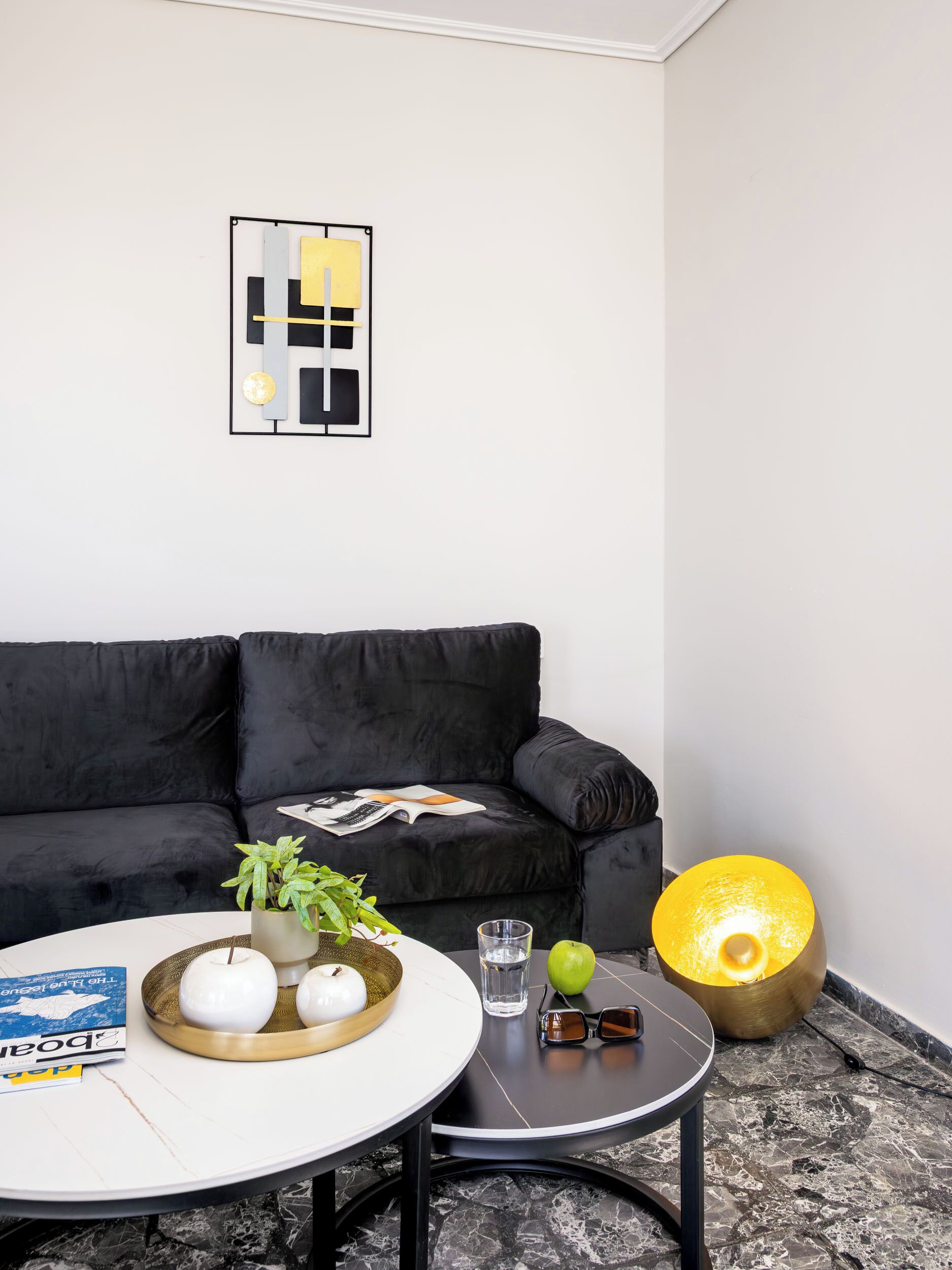Ein modernes Wohnzimmer mit einer schwarzen Couch, einem runden Couchtisch mit Dekoration, einer Stehlampe und einem minimalistischen Wandbild.