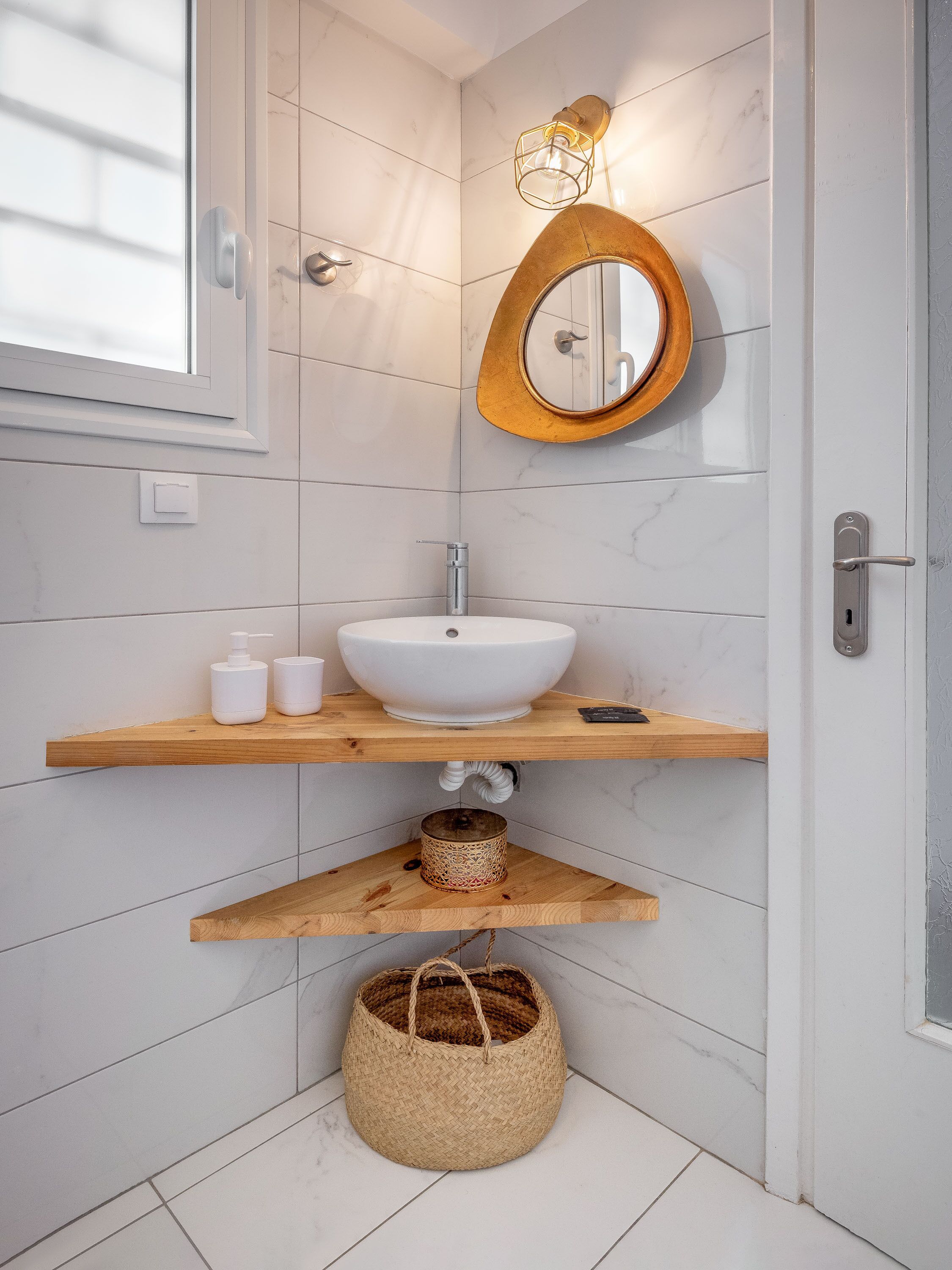 A modern bathroom with a white sink, wooden shelves, a round mirror, and a light fixture.