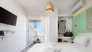 A modern hotel room with a bed, a TV, a hanging light fixture, and a view through a window. - Seaside Secret by BluPine (Vari-Voula-Vouliagmeni)