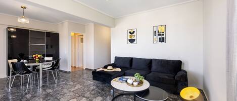 A modern living room with a black sofa, a round coffee table, and a dining area with a white table and black chairs.
