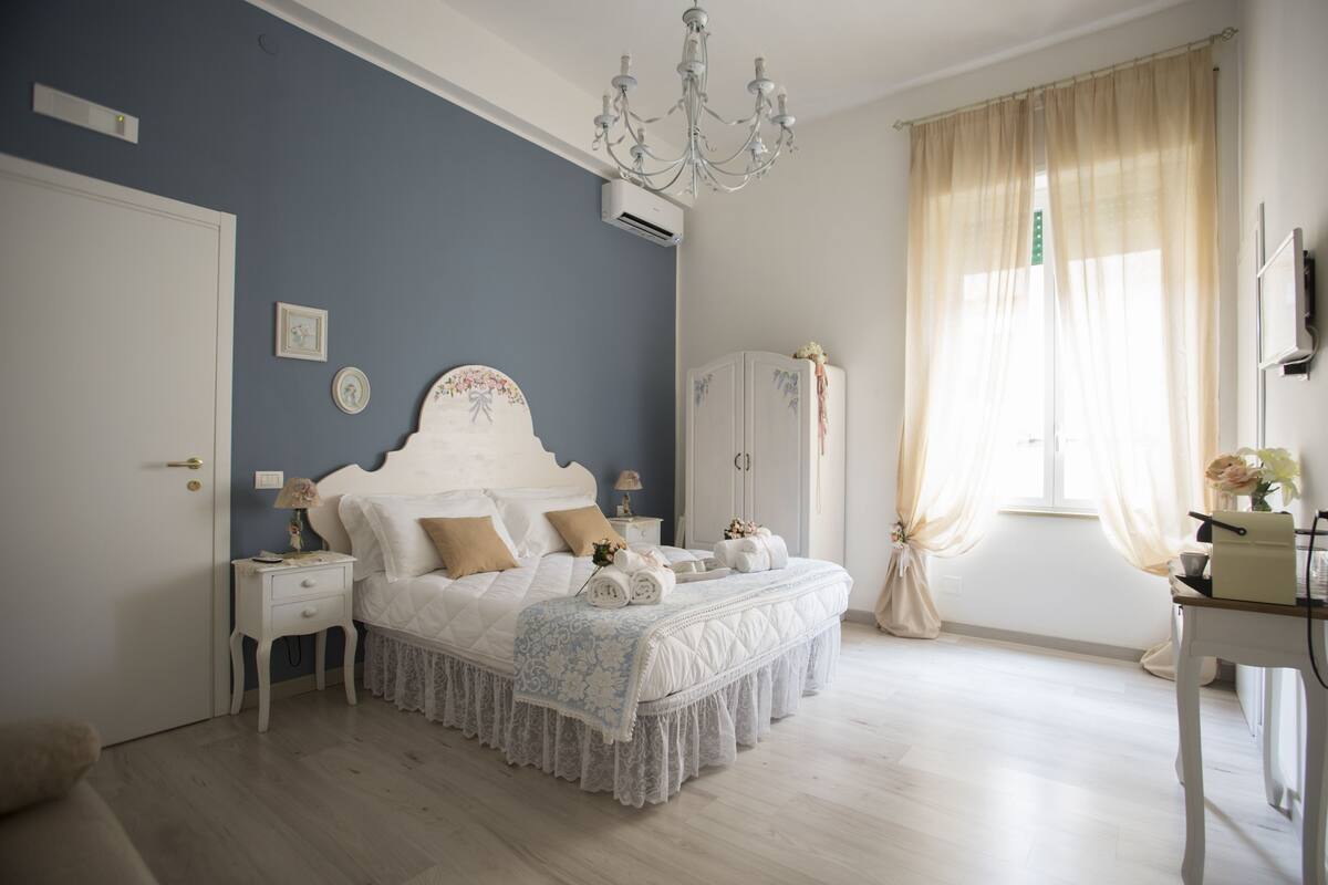A bedroom with a bed, bedside tables, a wardrobe, a desk, and a chandelier.