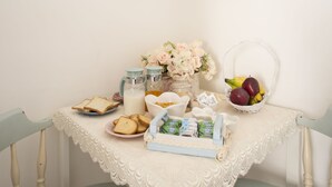 A dining table with a lace tablecloth, a basket of fruit, a vase of flowers, and various food items. - La Maison Romantique (Naples)