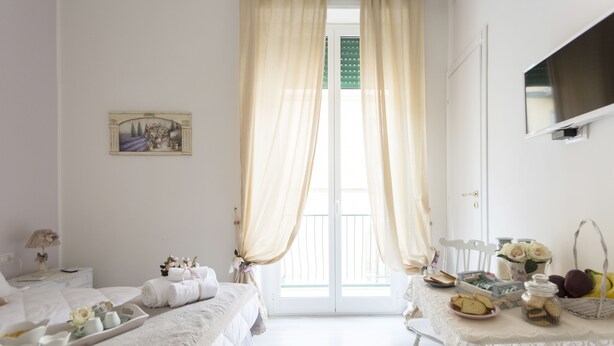 A hotel room with a bed, a table with breakfast items, and a balcony with curtains. - La Maison Romantique (Naples)