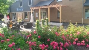 Hotellissa on katettu ulkoalue, jossa on istumapaikkoja, puutarha, jossa kasvaa vaaleanpunaisia kukkia, ja kyltti, joka osoittaa ravintolan sijainnin.