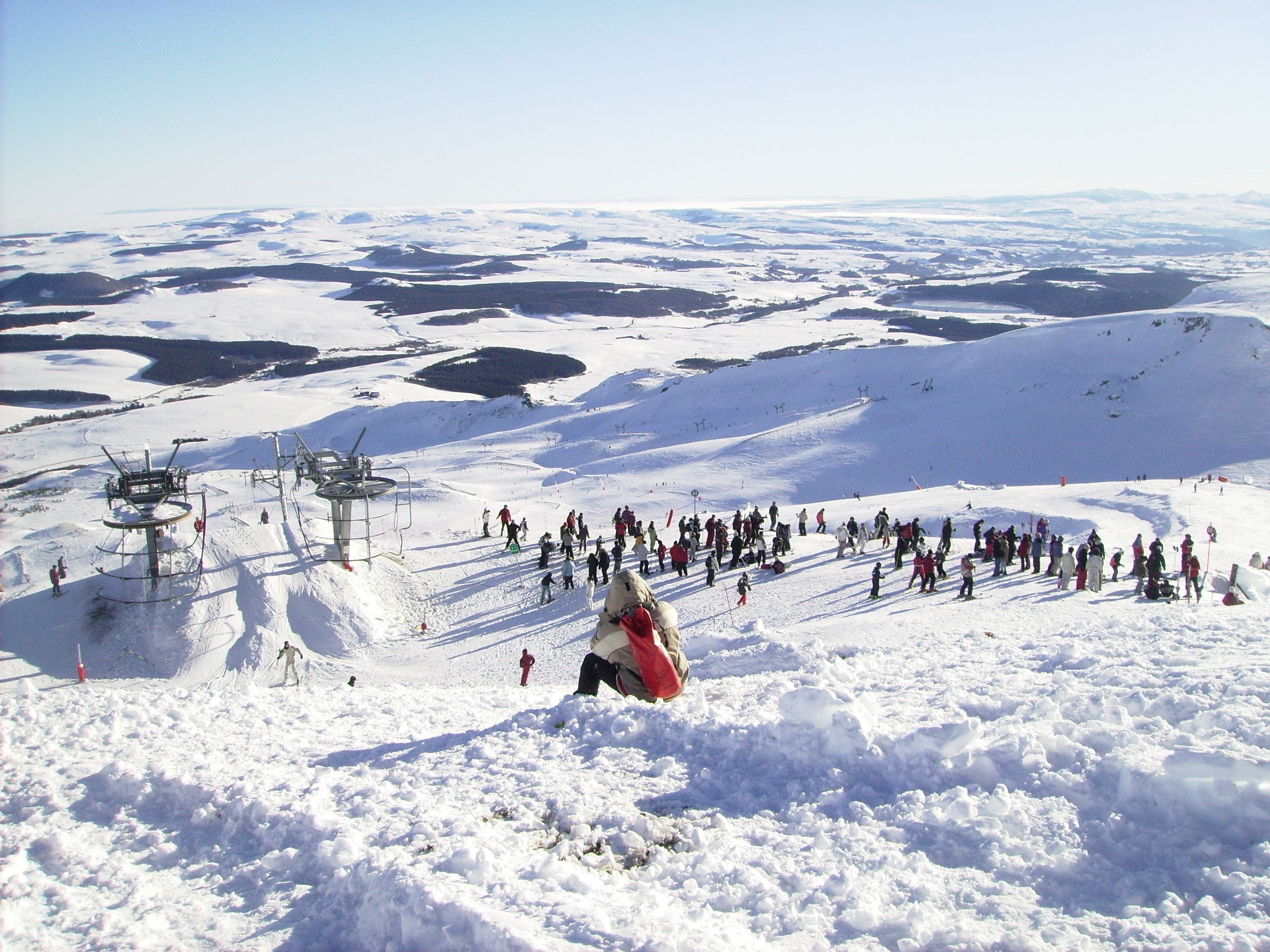Et sneklædt skiområde med stolelift og mange mennesker.