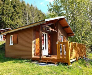 A small wooden cabin with a porch, a door, and a window. - Camping Bois de Gravière (Besse-et-Saint-Anastaise)