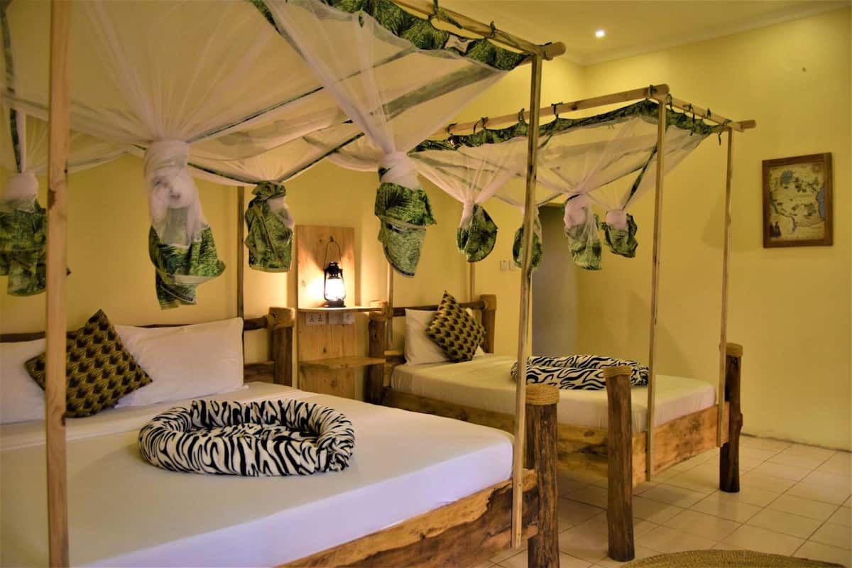 A room with two beds, each with a canopy bed frame and mosquito netting.