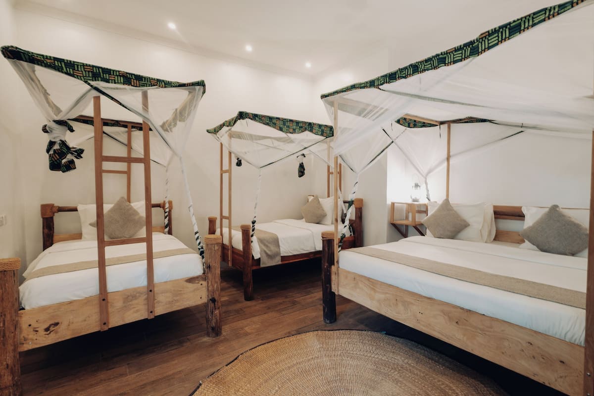 A room with three wooden beds, each with a canopy and a ladder. There is a woven rug on the floor.