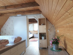 A bedroom with a sloped ceiling, wooden walls, a bed with floral bedding, a nightstand, a small cabinet, and a potted plant. - Ferienhof Cohrs - Ferienhäuser (Bispingen)