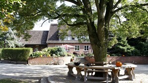 A courtyard with a stone bench, a tree, and a brick building in the background. - Ferienhof Cohrs - Ferienhäuser (Bispingen)