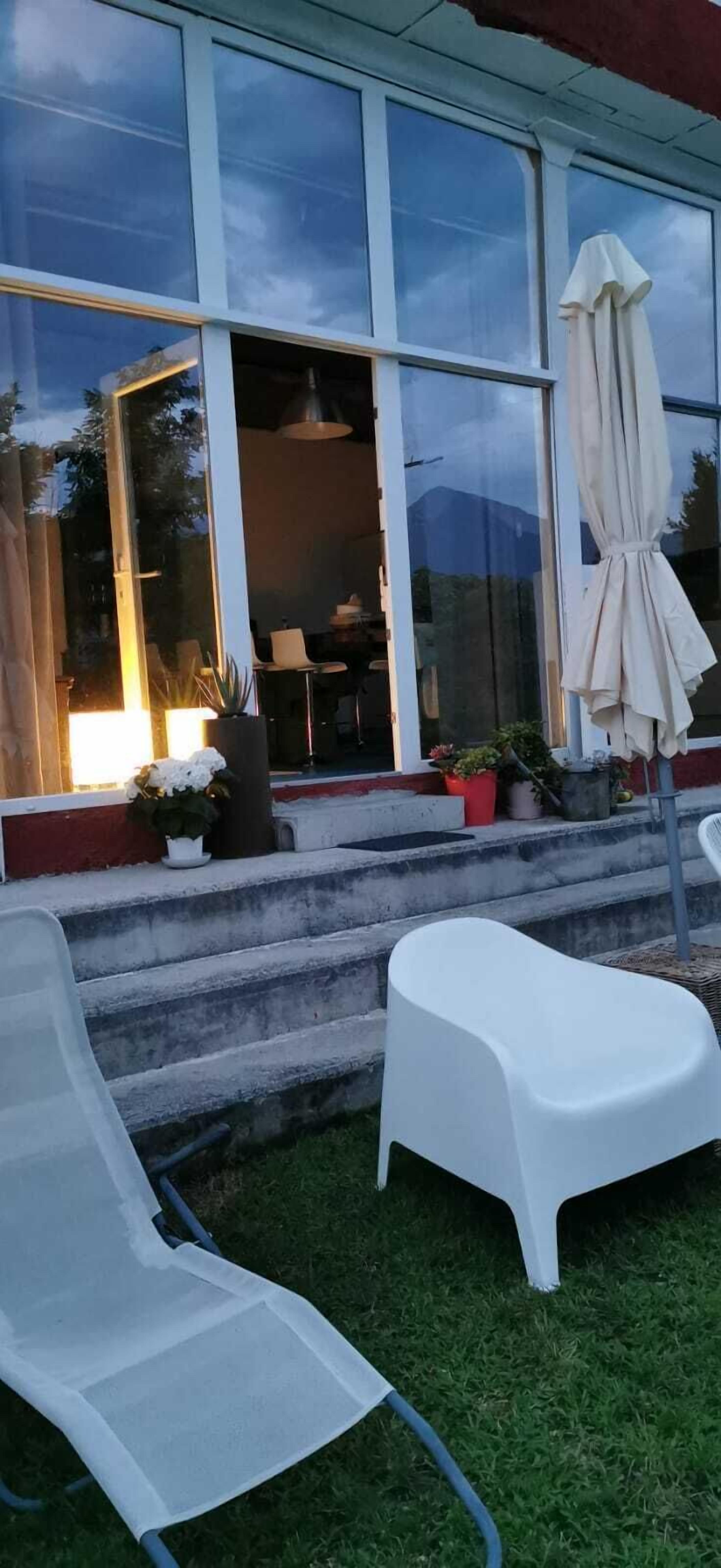 Una casa moderna con ventanas amplias, mobiliario exterior y plantas en macetas.