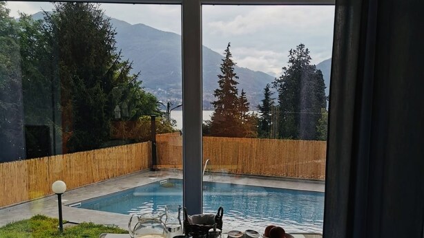 Comedor con una mesa preparada para dos personas, con vistas a una piscina y montañas.