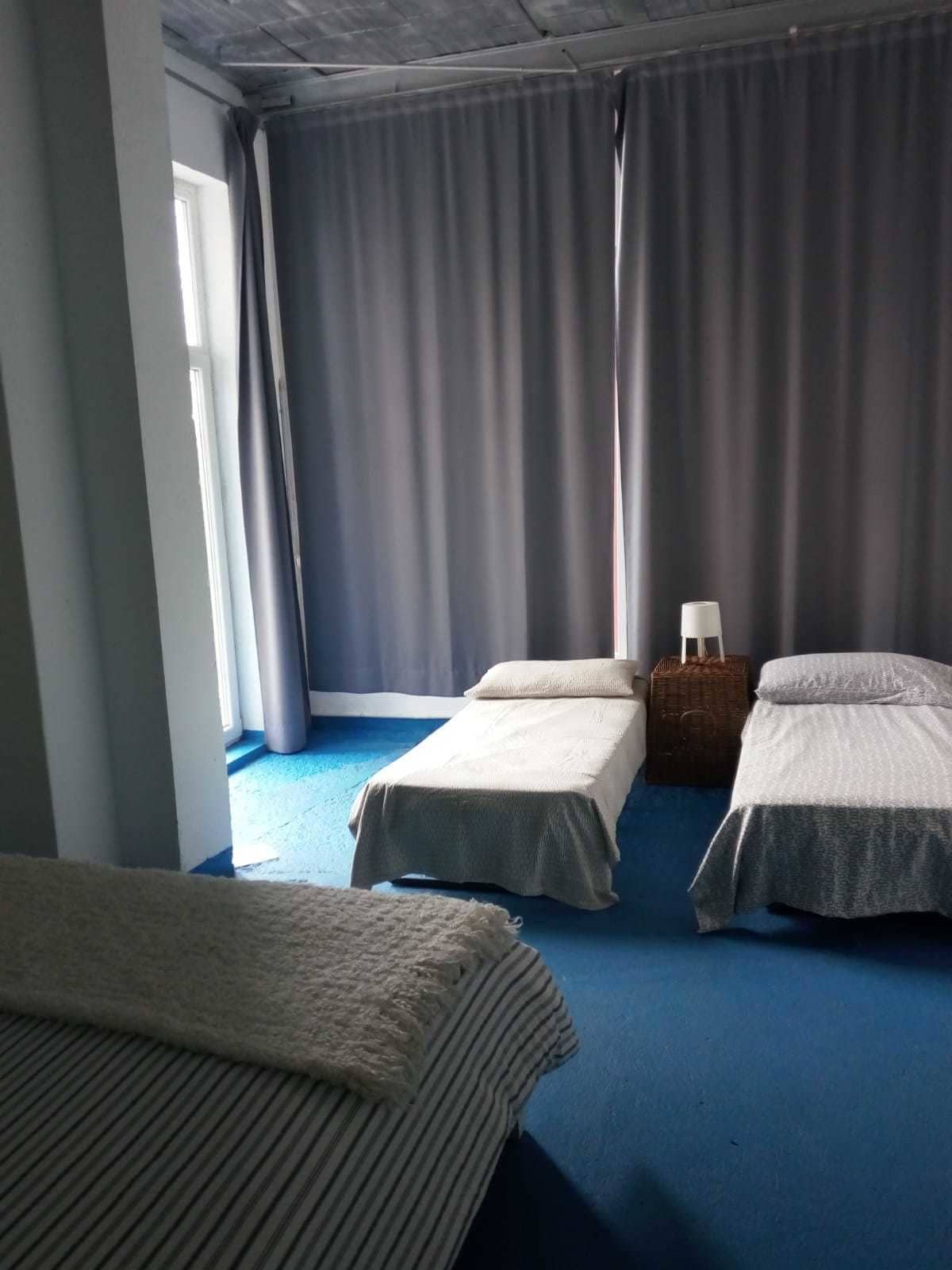 Ein Zimmer mit zwei Einzelbetten, einem kleinen Tisch mit Lampe und einem Fenster mit Vorhängen.