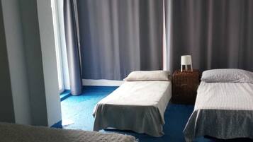 Ein Zimmer mit zwei Einzelbetten, einem kleinen Tisch mit Lampe und einem Fenster mit Vorhängen.