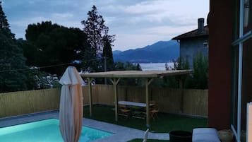 Un patio trasero con piscina, sillas de descanso y un pérgola.
