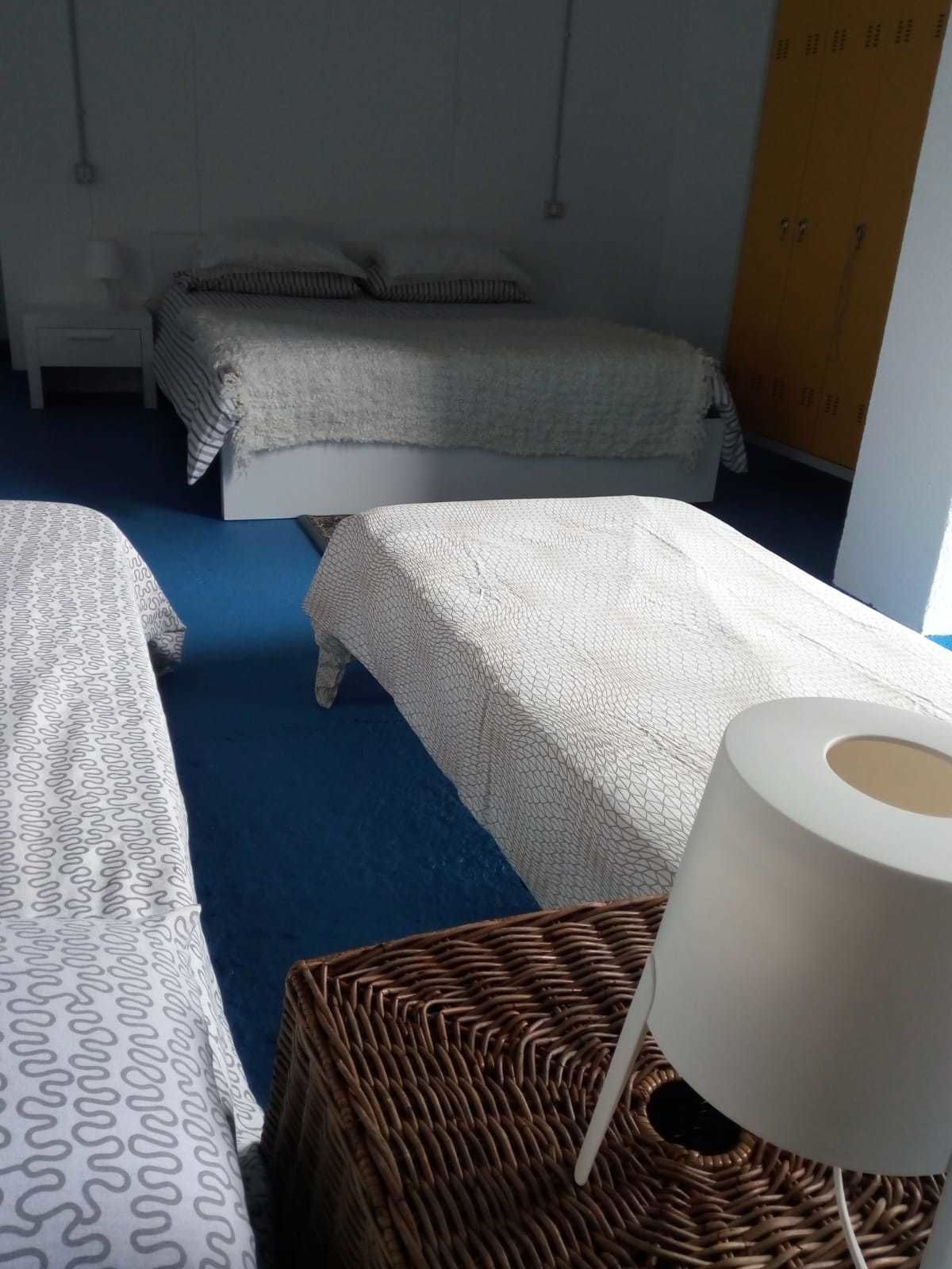 A hotel room with two beds, a wicker side table with a lamp, and a blue carpet.